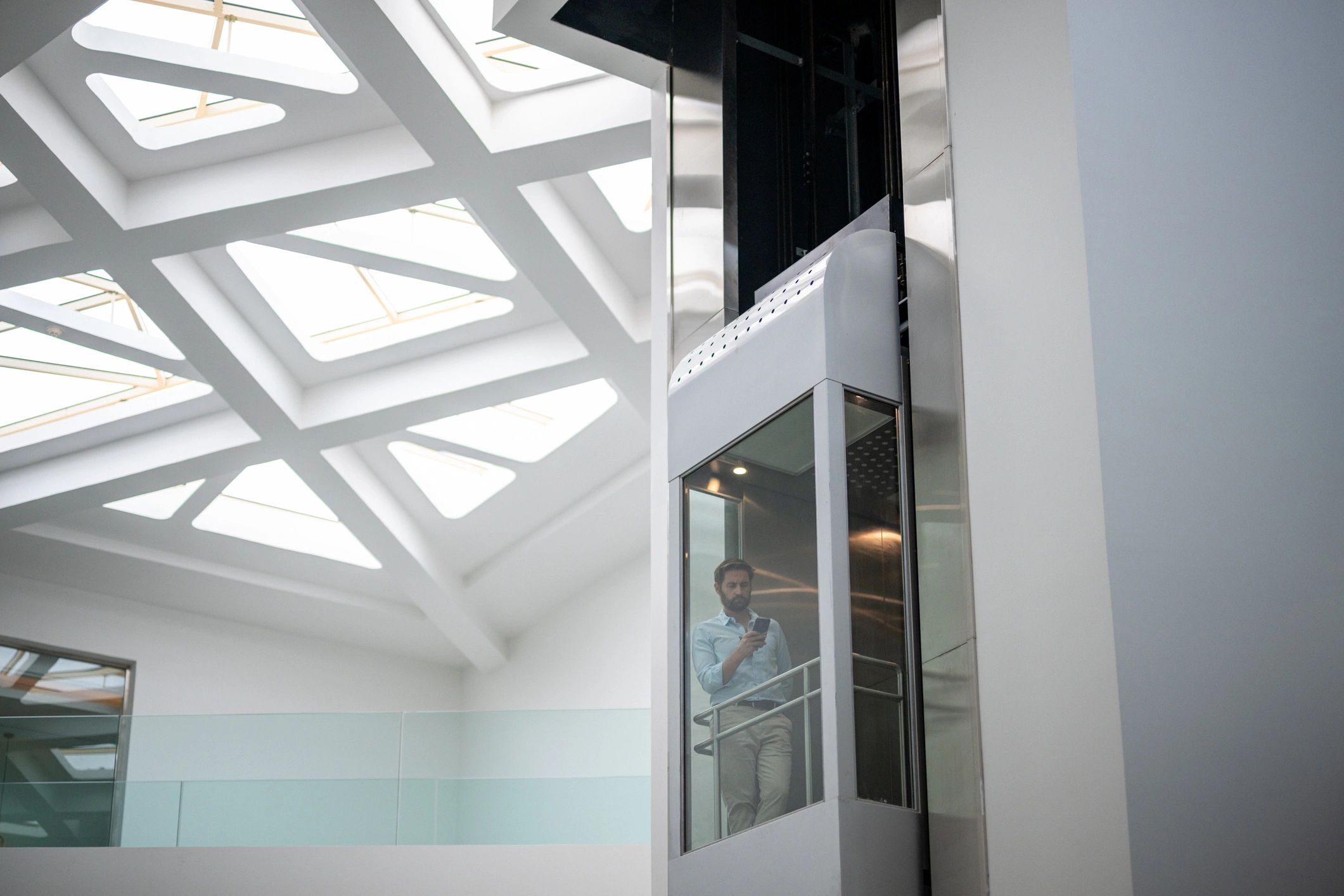 Wide shot of a modern hotel atrium with man in a glass elevator and a skylight ceiling with geometric beams